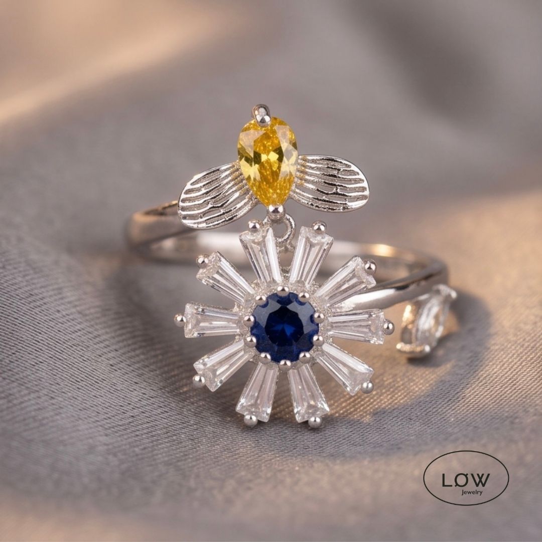 Sølvfarget justerbar fidget ring i kobber med roterende blomst og bie. Velg blå eller rosa blomsterkjerne. Fra LØW Jewelry.