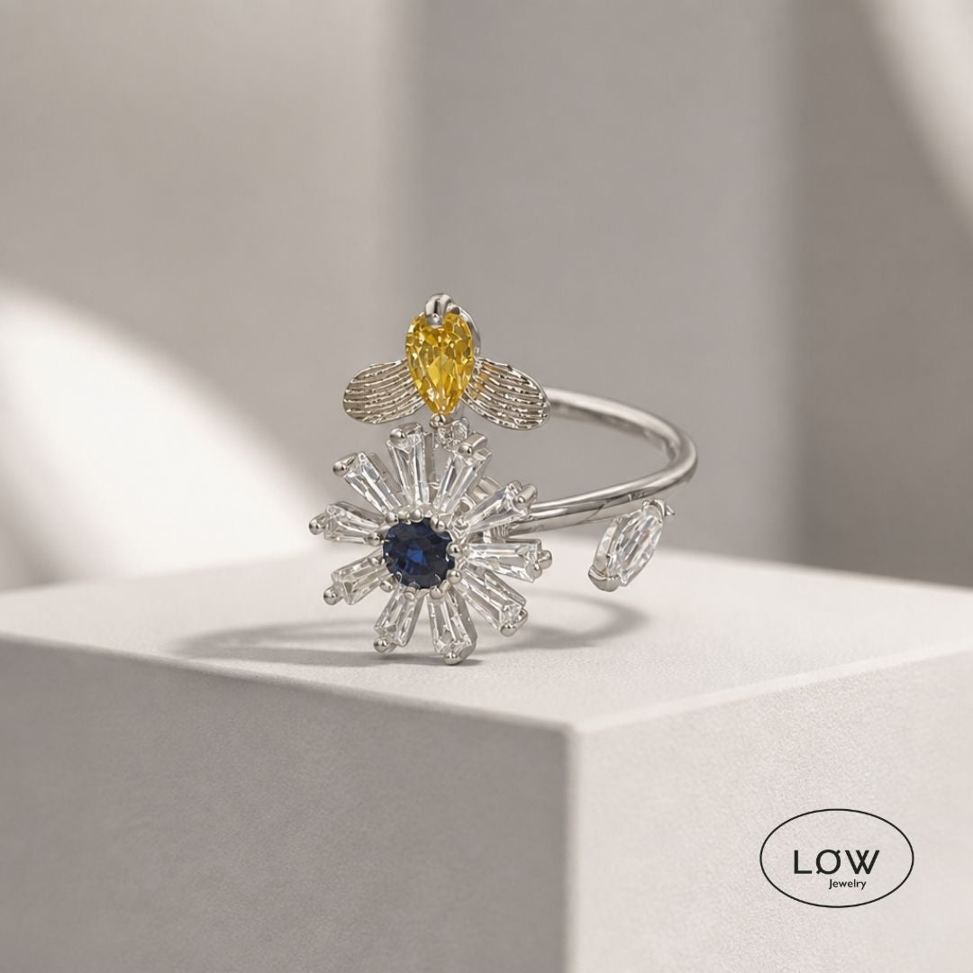 Sølvfarget justerbar fidget ring i kobber med roterende blomst og bie. Velg blå eller rosa blomsterkjerne. Fra LØW Jewelry.