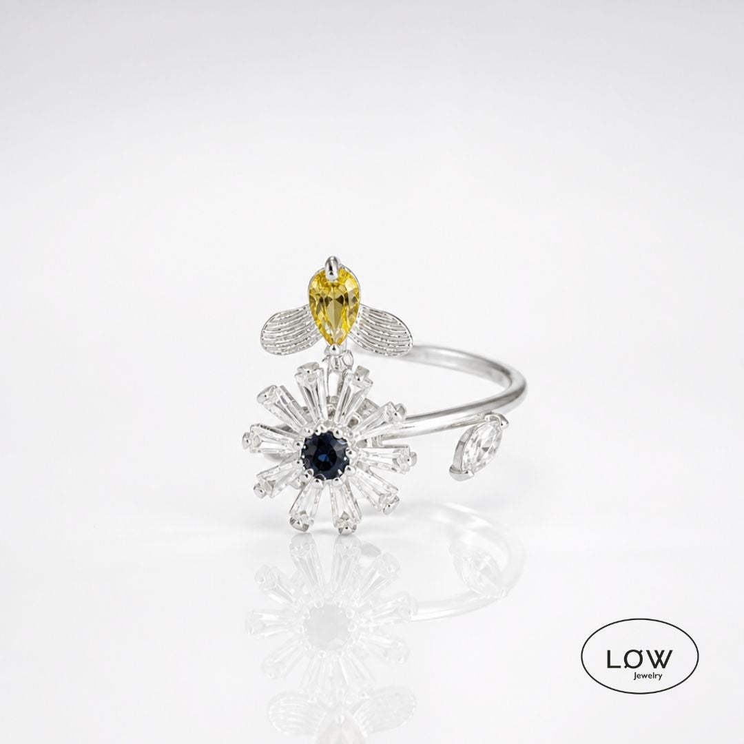 Sølvfarget justerbar fidget ring i kobber med roterende blomst og bie. Velg blå eller rosa blomsterkjerne. Fra LØW Jewelry.