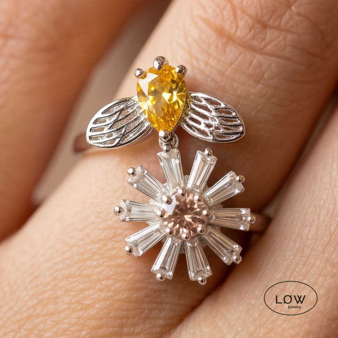 Sølvfarget justerbar fidget ring i kobber med roterende blomst og bie. Velg blå eller rosa blomsterkjerne. Fra LØW Jewelry.