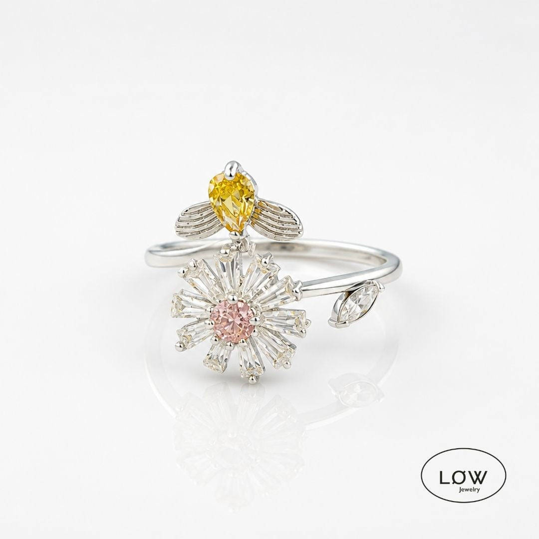 Sølvfarget justerbar fidget ring i kobber med roterende blomst og bie. Velg blå eller rosa blomsterkjerne. Fra LØW Jewelry.